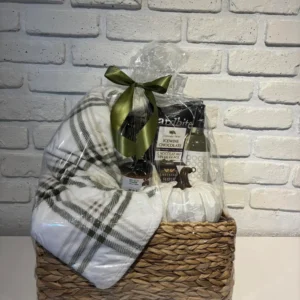 Fall gift basket in a woven basket with a plaid throw, decorative white pumpkin, brie, icewine chocolate and white wine