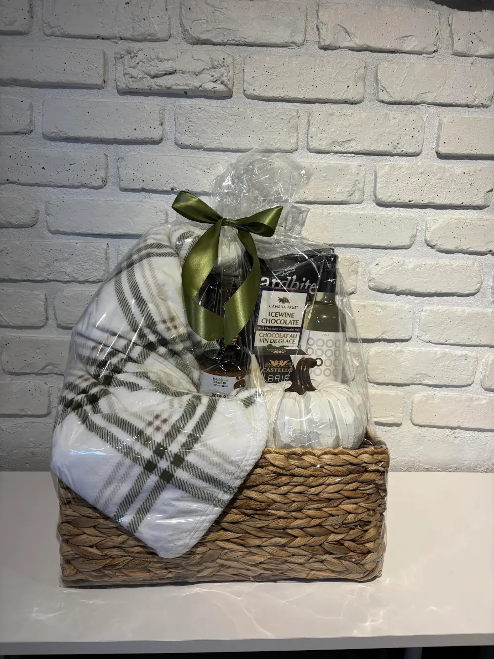 Fall gift basket in a woven basket with a plaid throw, decorative white pumpkin, brie, icewine chocolate and white wine