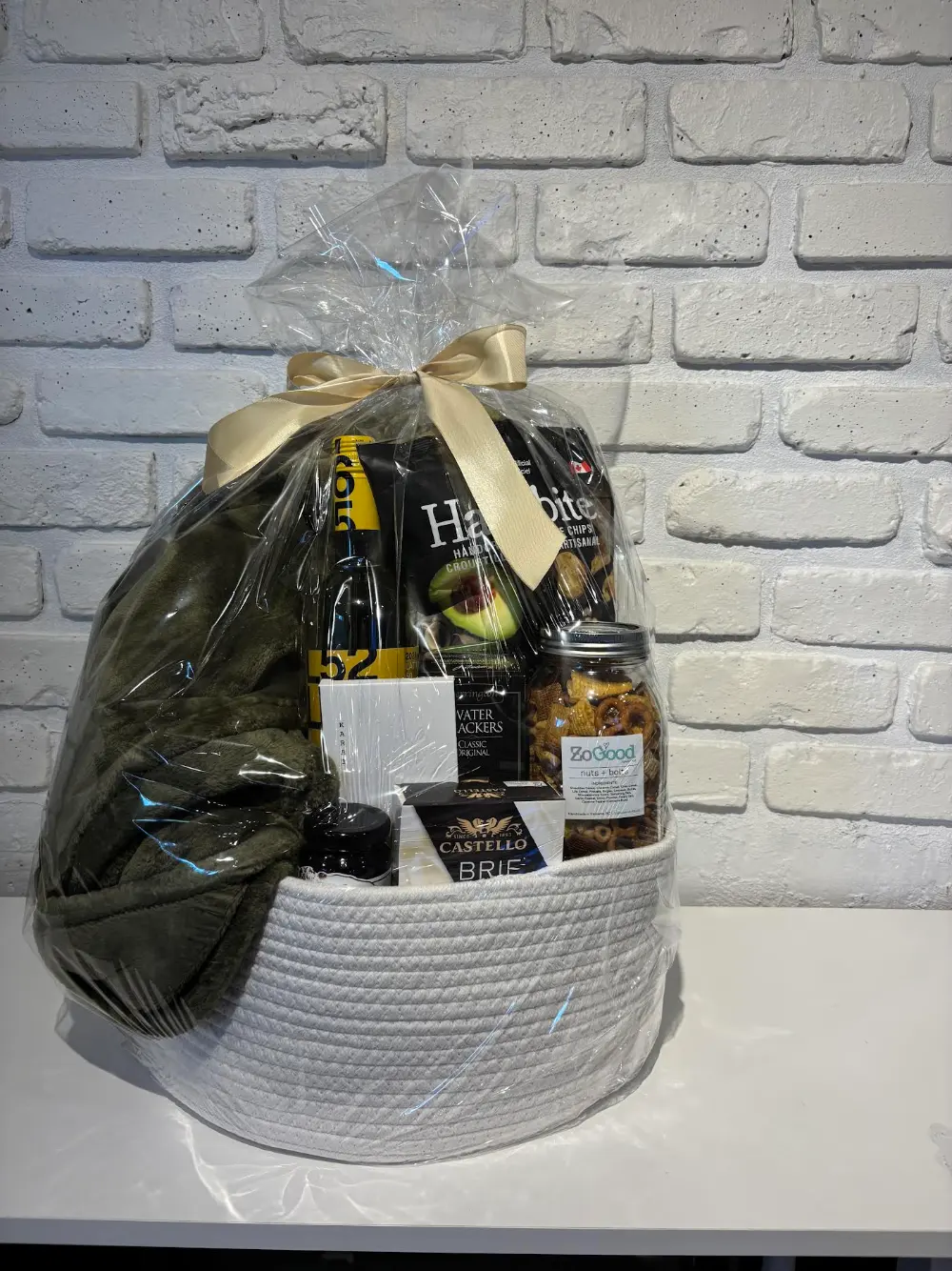 White cotton rope basket gift set with a cozy green throw, Latitude 50 white wine, Castello brie, water crackers and local BC snacks