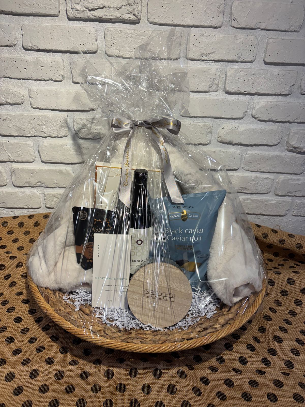 Large Rattan Gift Basket with a cozy white throw, red wine, a Watson's candle, Karat chocolate and Black Caviar potato crisps